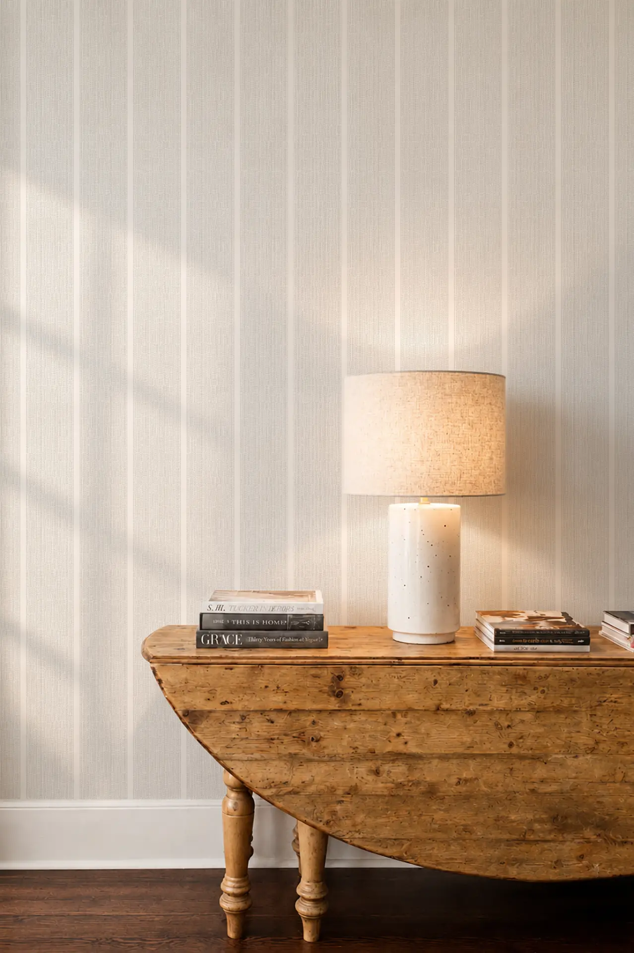 Sandbar wallcovering in Driftwood behind a wooden drop-leaf console with books and a lit ceramic table lamp.